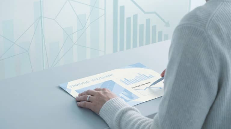 Une personne analyse un document financier montrant une tendance à la baisse des frais sur un bureau moderne.